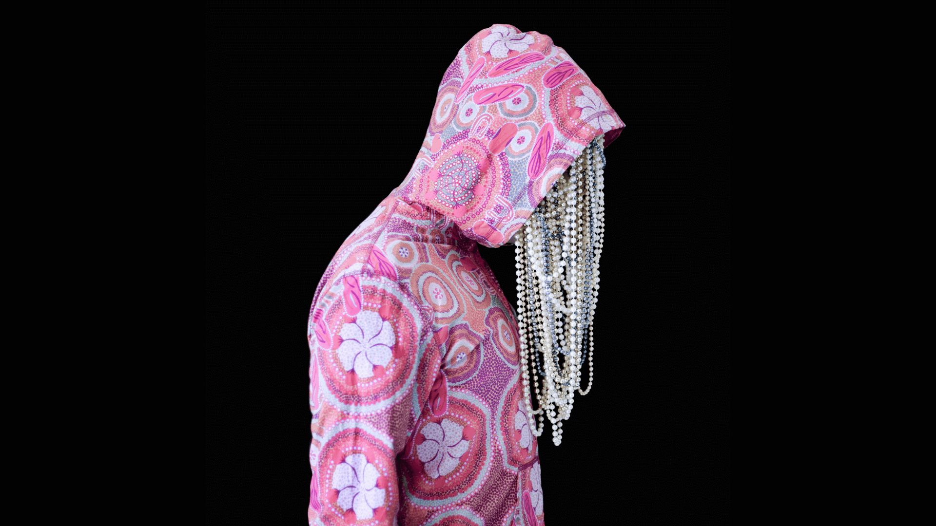 A person poses in profile with a hood drawn up and head down. From the face strings of pearls drop down.